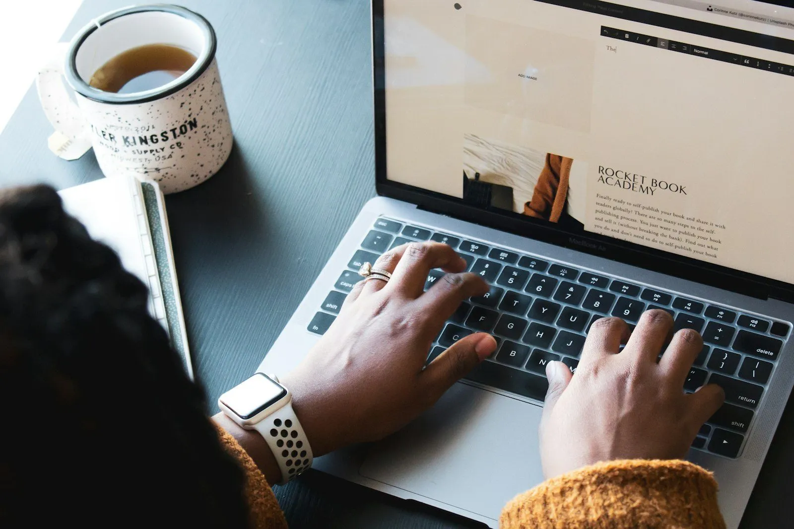 Osoba pracująca na laptopie przy stole, obok kubek z kawą